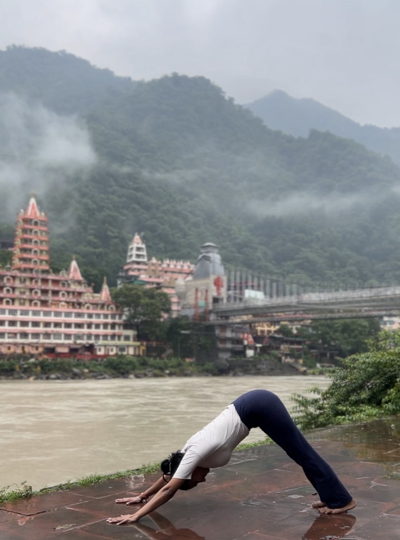 Downward dog on the riverbank with Laxman Jhula behind, Rishikesh
